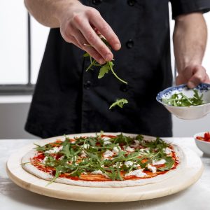 man-putting-arugula-pizza-dough